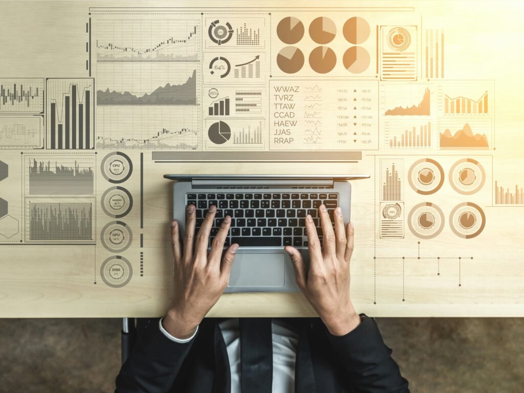 An overhead photo of a man sitting with only a portion of his jacket, shirt and tie visible, and his hands hovering slightly above the keyboard of a laptop. Various graphics – such as charts, dashboards, performance indicators and more – have been added to the desk to suggest the range of data the man has access to through his laptop screen. Anthony Lambert, in his interview, describes how he eventually became a FileMaker developer.